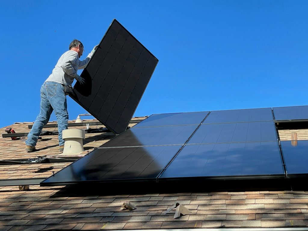 man standing on roof placing black solar panel